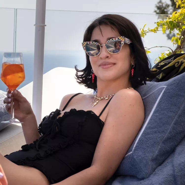A woman with a bob haircut sitting in a lounge chair holding a drink. 