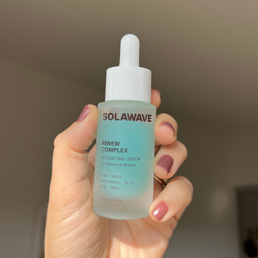 Solawave Renew Complex Activating Serum held up in a woman's hand.
