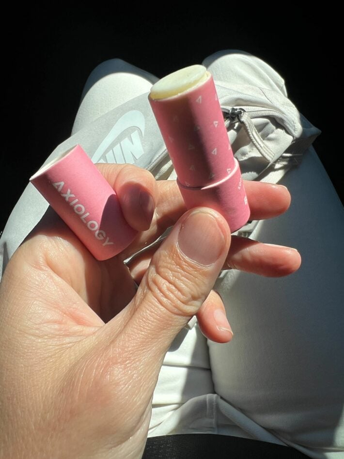 A woman holding up a tube of lip balm by Axiology.