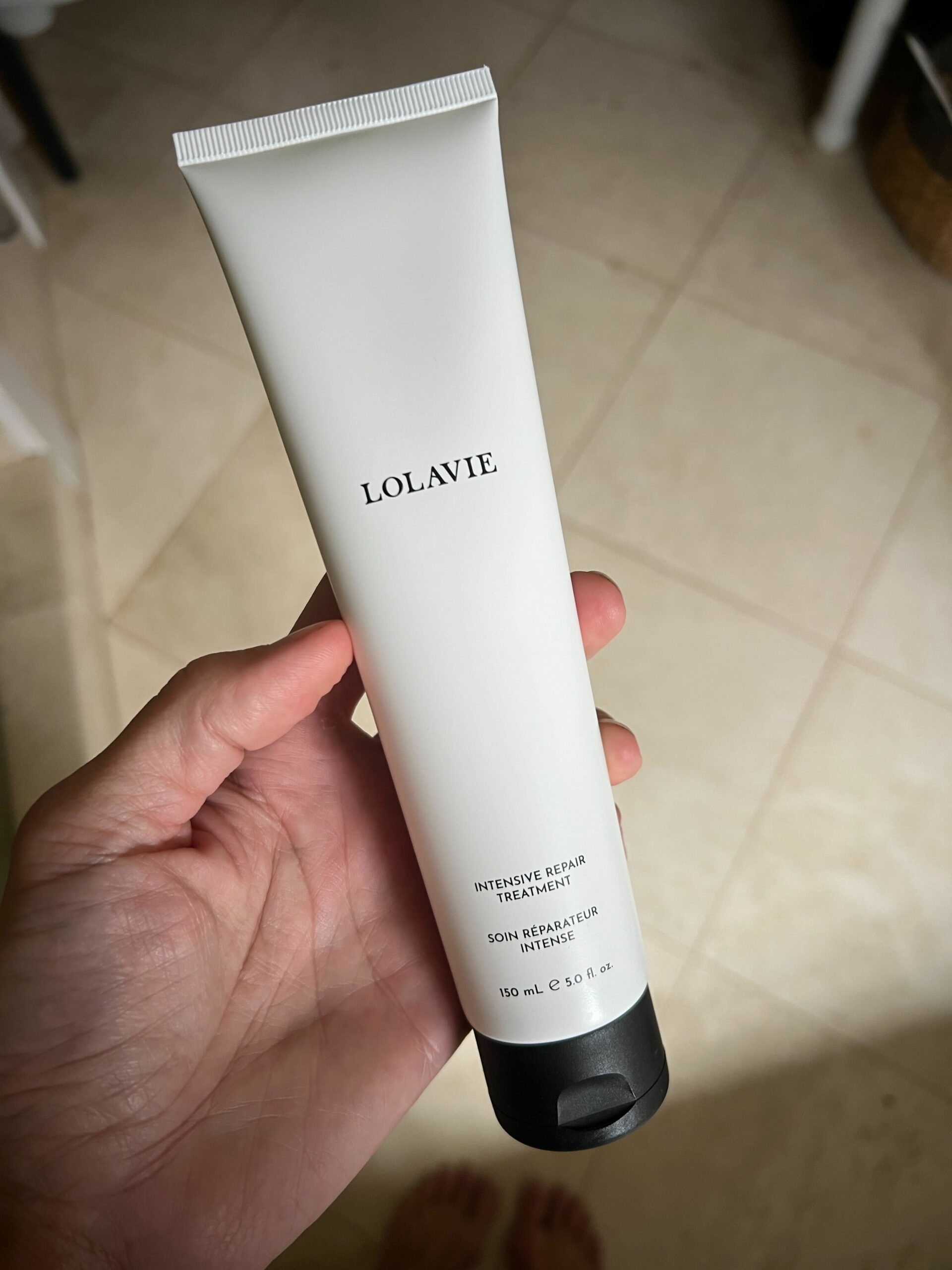 A bottle of LolaVie's Intensive Repair Treatment in a woman's hand.