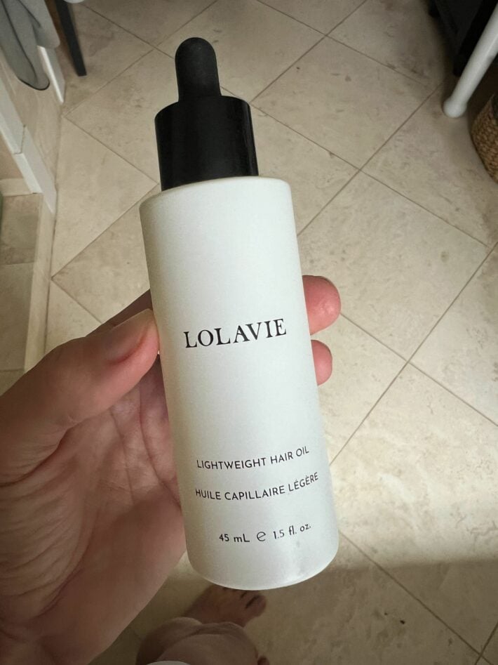 A bottle of LolaVie's Lightweight Hair Oil in a woman's hand.