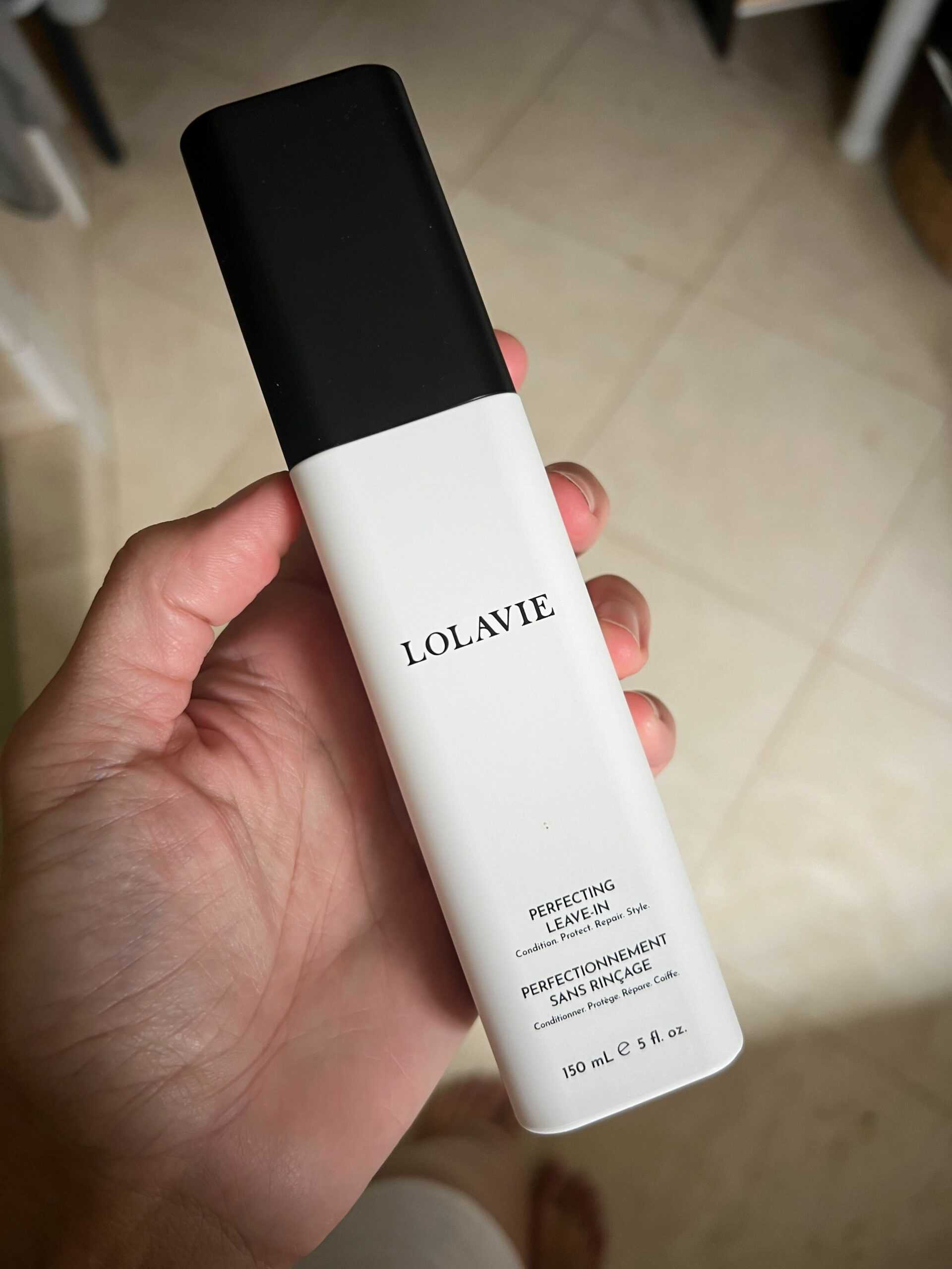 A bottle of LolaVie's Perfecting Leave-In in a woman's hand.
