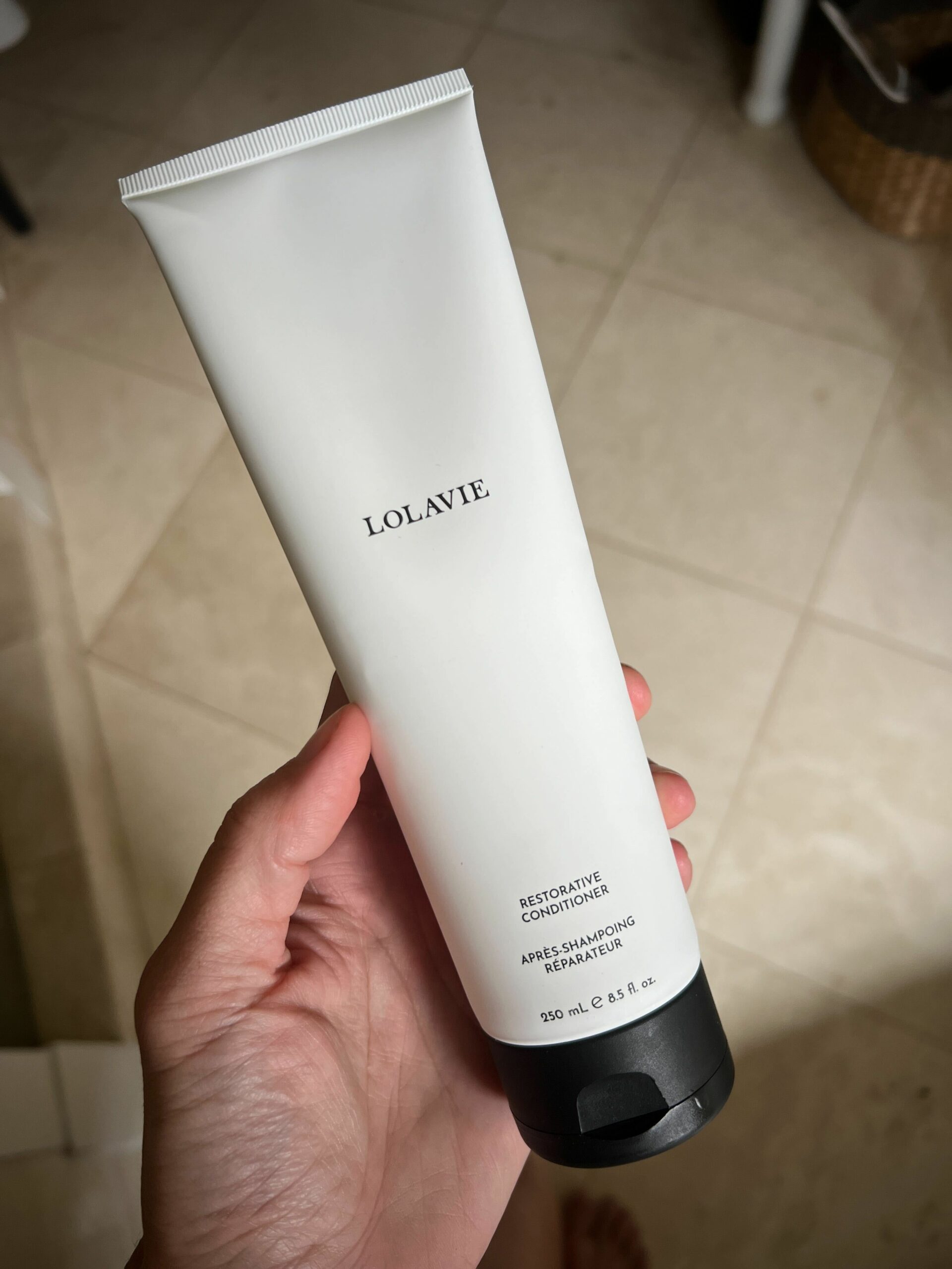 A bottle of LolaVie's Restorative Conditioner in a woman's hand.