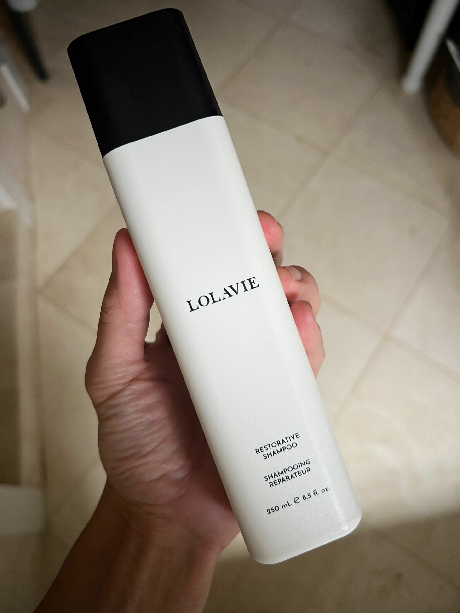 A bottle of LolaVie's Restorative Shampoo in a woman's hand.