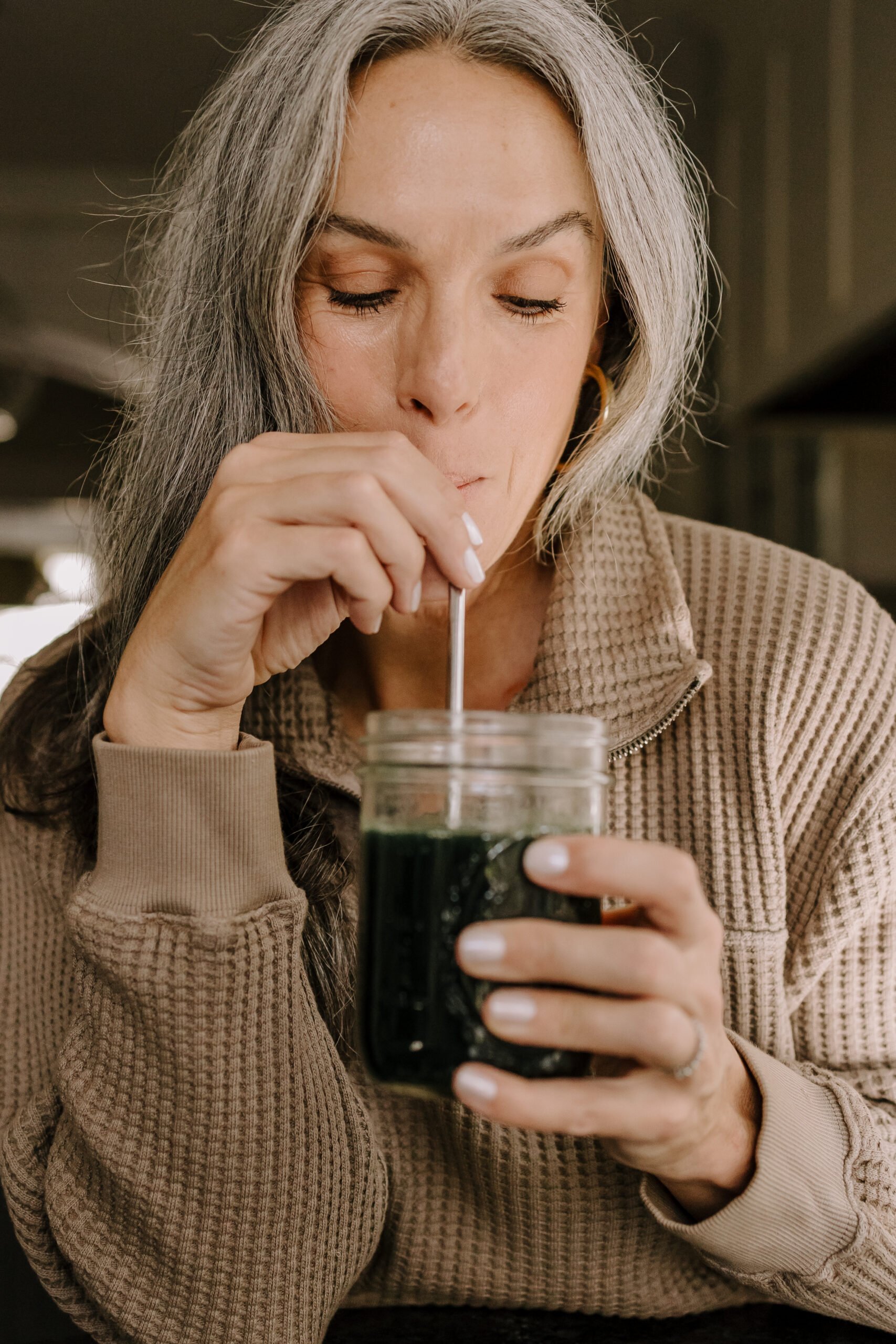A woman drinking greens from a glass.