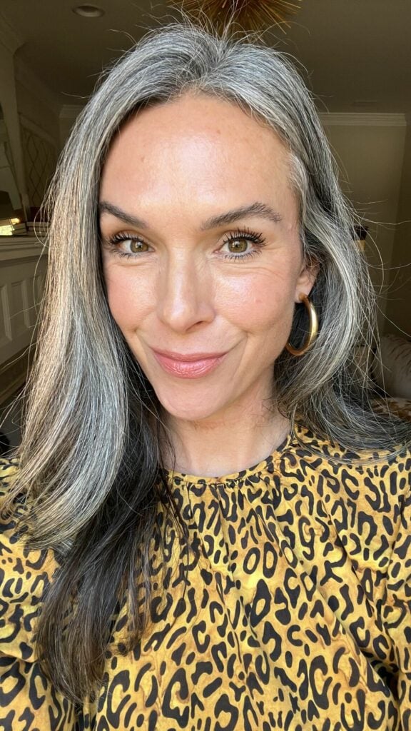 A woman in a yellow leopard print top with long gray hair.