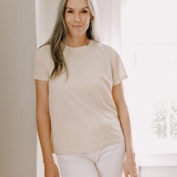 A woman wearing at MATE the Label t-shirt leans against a doorway.