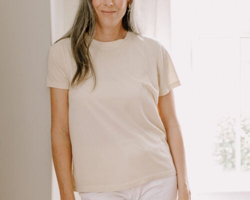 A woman wearing at MATE the Label t-shirt leans against a doorway.