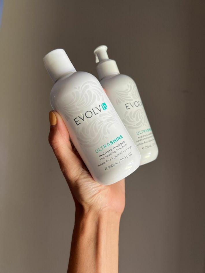 A hand holding up EVOLVh shampoo and conditioner. 