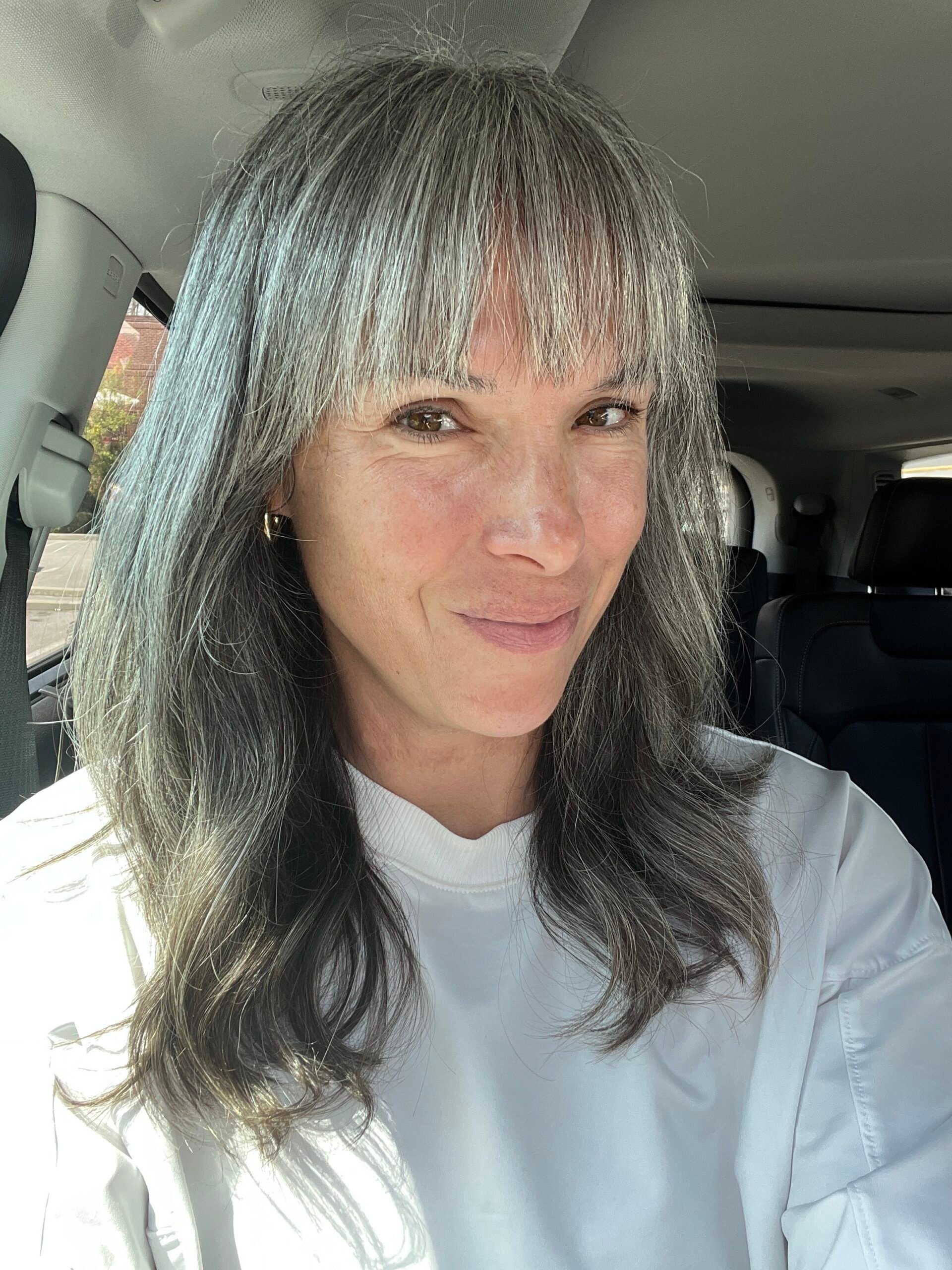 A woman with long gray hair sits in her car.