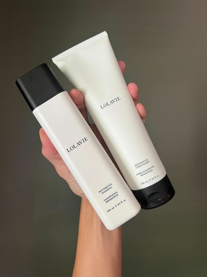 A hand holding up LolaVie shampoo and conditioner.