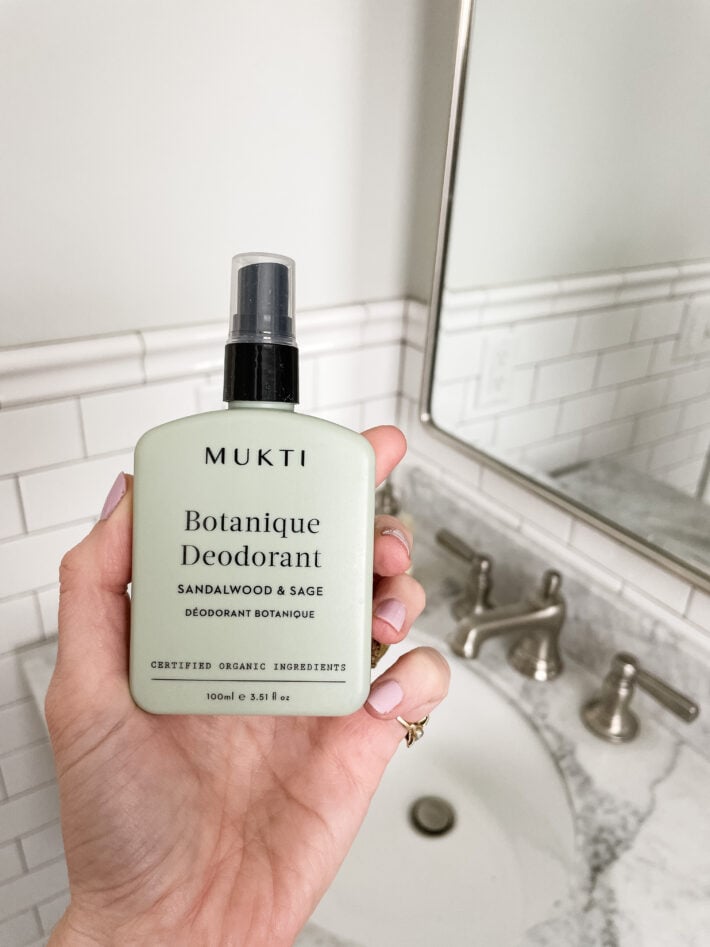 A bottle of Mukti deodorant held up in front of a sink.