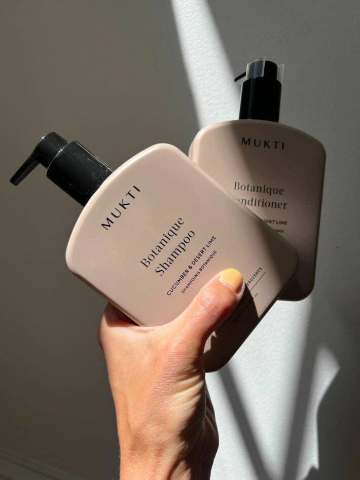 A hand holding up Mukti shampoo and conditioner. 
