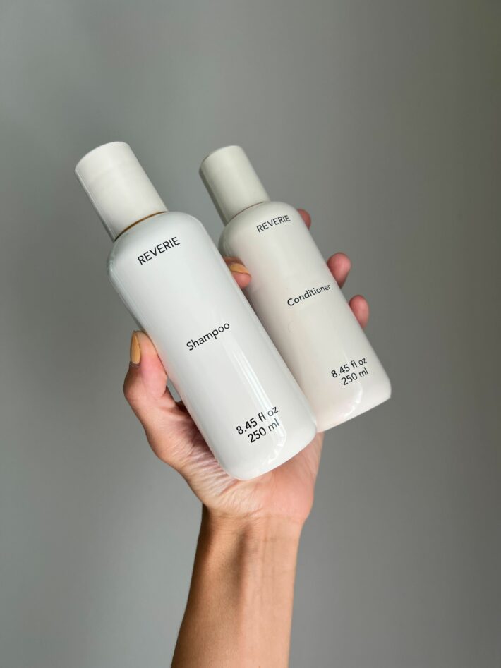A hand holding up REVERIE shampoo and conditioner.