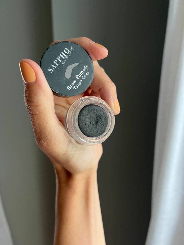 Sappho Brow Pomade held up in a hand.