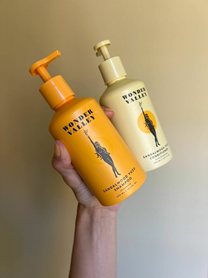 A hand holding up WONDER VALLEY shampoo and conditioner.