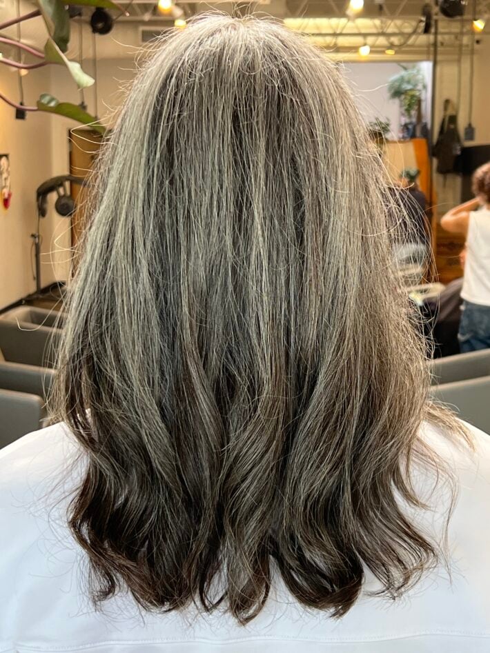 A close up of up of the backside of a woman's head of hair showing her long wavy gray hair.