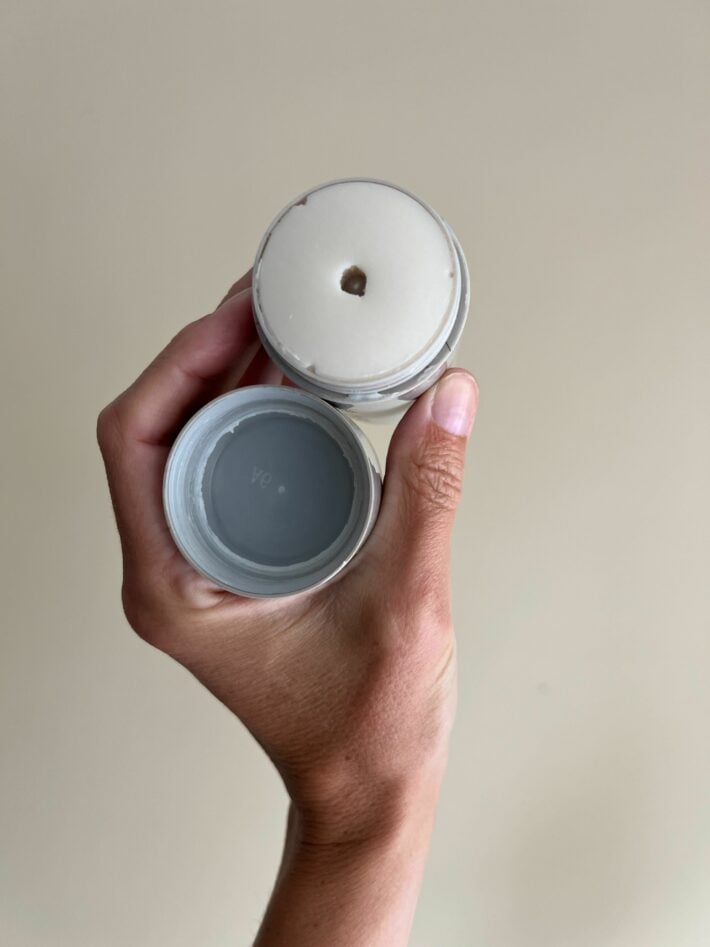 A tube of deodorant held up in a hand with the lid off. 