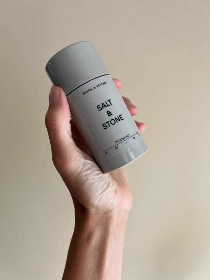 A container of SALT + STONE Santal & Vetiver Natural Deodorant held up in a hand.